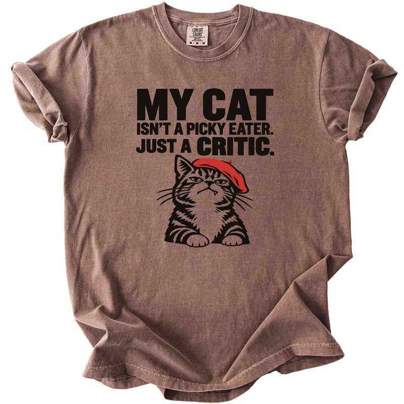 Brown t-shirt with black text and a cartoon cat wearing a red beret.