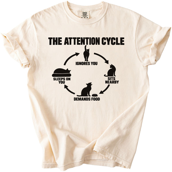 Cream t-shirt with black graphic "The Attention Cycle" featuring cat illustrations and text.