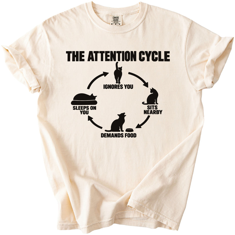 Cream t-shirt with black graphic "The Attention Cycle" featuring cat illustrations and text.
