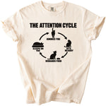 Cream t-shirt with black graphic "The Attention Cycle" featuring cat illustrations and text.