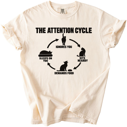 Cream t-shirt with black graphic "The Attention Cycle" featuring cat illustrations and text.