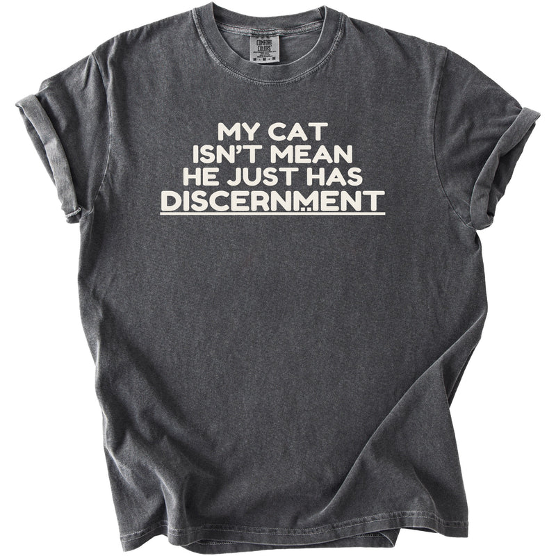 Dark grey t-shirt with white text reading "MY CAT ISN'T MEAN HE JUST HAS DISCERNMENT"